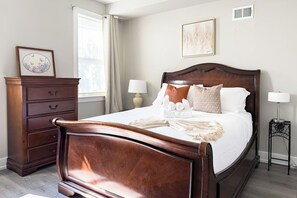 Un lit bien fait, avec des oreillers et une couverture, une commode en bois avec des tiroirs, une table de chevet avec une lampe et une fenêtre avec des rideaux.