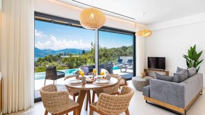 Una sala moderna con comedor, televisor y vistas a una piscina y montañas.