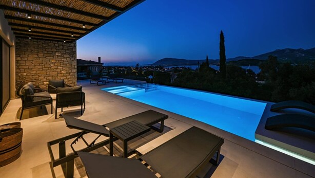 Piscina infinita al aire libre con pared de piedra y mobiliario, con vistas a un paisaje montañoso.
