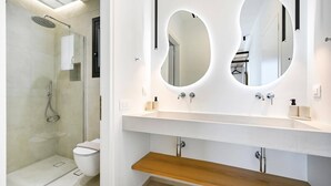 Un baño moderno con cabina de ducha de vidrio, inodoro y tocador con dos espejos.