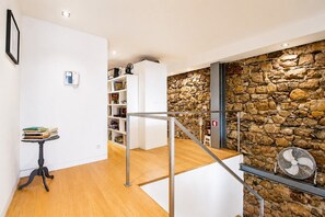 A modern interior with a wooden floor, white walls, a stone wall, a staircase, and a fan. - A Varanda do Tempo Apartment: Archaeology, History, Terrace & Wi-Fi in Central Coimbra (Coimbra)