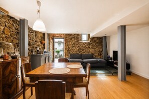 A dining area with a wooden table and chairs, a stone wall, a sofa, and a television. - A Varanda do Tempo Apartment: Archaeology, History, Terrace & Wi-Fi in Central Coimbra (Coimbra)