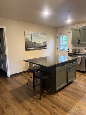 A kitchen with a central island, bar stools, a window, and a door.