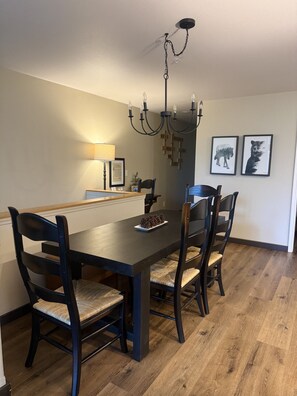 A dining area with a wooden table, four chairs, a chandelier, and framed animal prints on the wall.