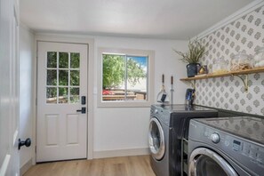 Une buanderie équipée d’un lave-linge, d’une porte avec une fenêtre et d’une étagère contenant divers objets.