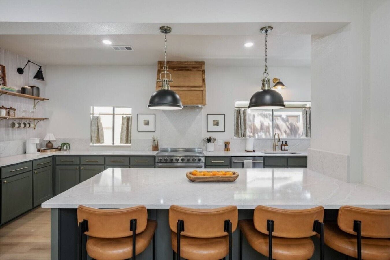 A modern kitchen with a large island, dark pendant lights, and a central stove.