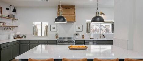 A modern kitchen with a large island, dark pendant lights, and a central stove.