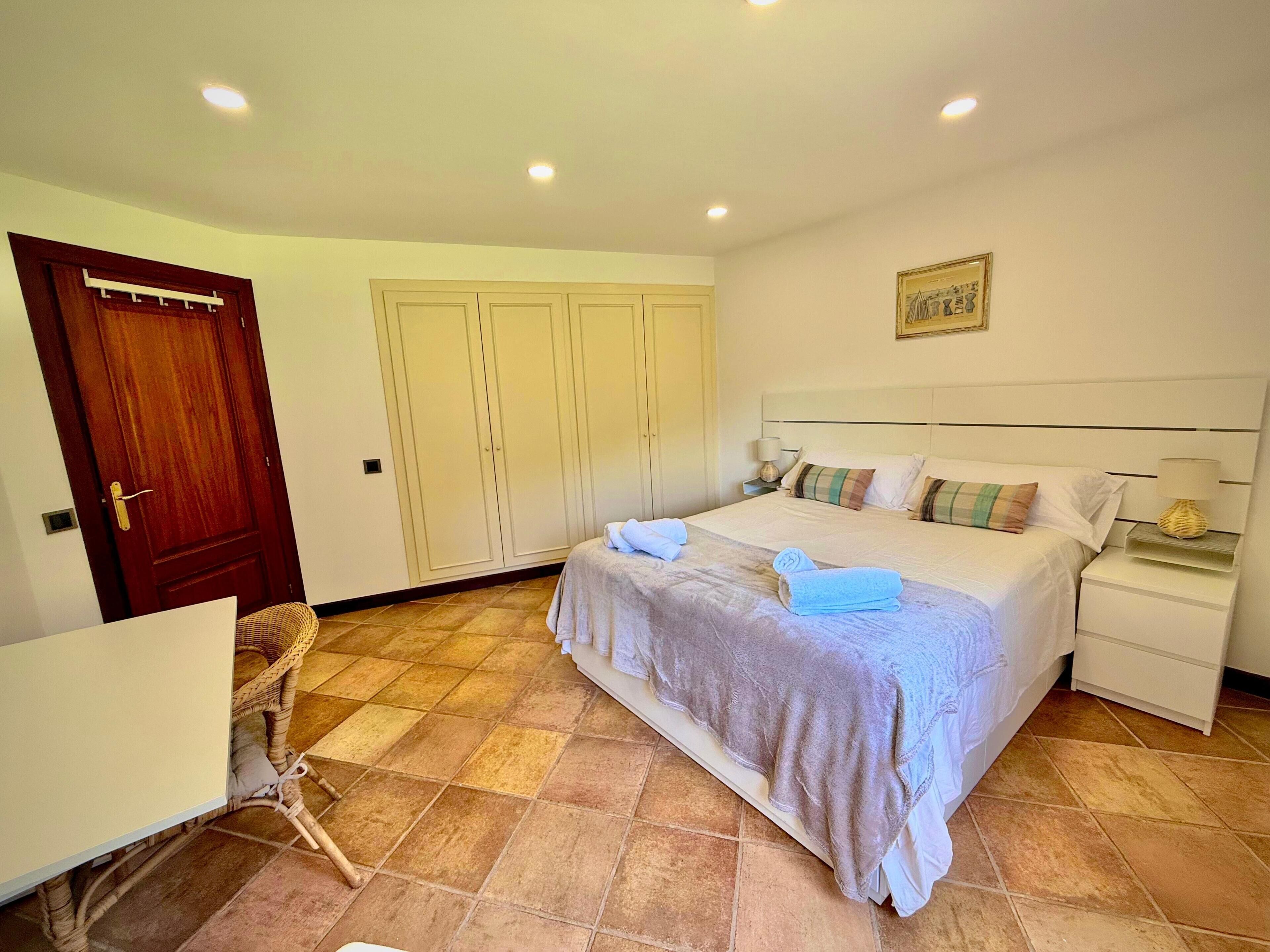 A bedroom with a bed, bedside tables, a wardrobe, a desk, and a chair.