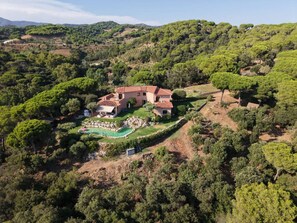 Una casa grande con piscina rodeada de exuberante vegetación y colinas.