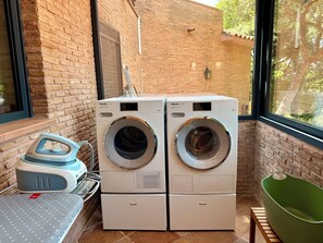 Two white Miele washing machines in a laundry area with a brick wall, a window, and a green chair. - Seaview Villa * Pool * Beach * Barcelona Coast (Sant Pol de Mar)