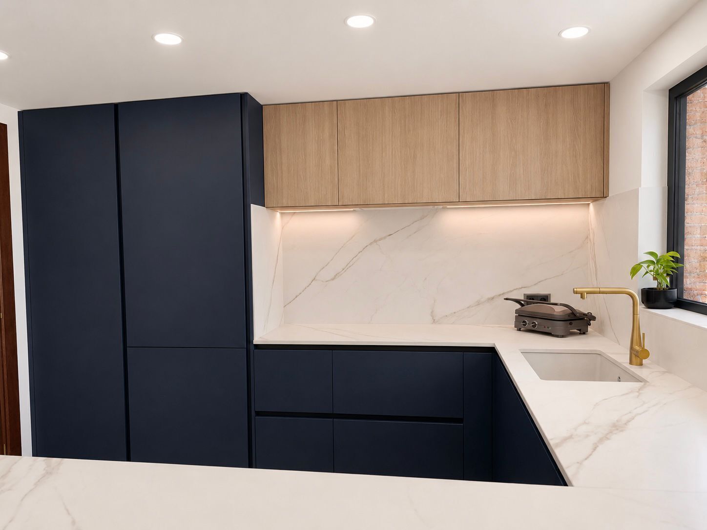 A modern kitchen with dark cabinetry, a marble countertop, and a gold faucet.