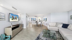 A modern living room with a glass coffee table, a white sofa, and a dining area with a white table and chairs. - Top Floor Gulf View Condo at South Seas Tower IV. (Marco Island)