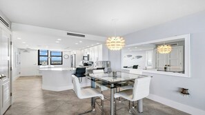 A modern kitchen with a central island, white cabinetry, and a dining area with a glass table and white chairs. - Top Floor Gulf View Condo at South Seas Tower IV. (Marco Island)