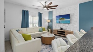 Ein modernes Wohnzimmer mit Sofa, Couchtisch, Fernseher und Deckenventilator.