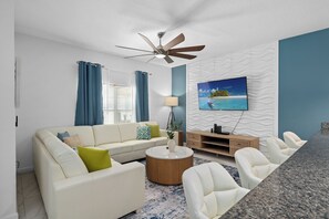 A modern living room with a sofa, coffee table, TV, and a ceiling fan. - Lakeview Pool Townhome in Storey Lake Resort • Lazy River • 8 Miles to Disney (Kissimmee)