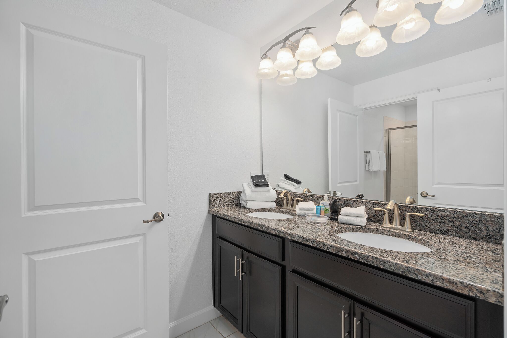A bathroom with a double sink, dark cabinets, a large mirror, and a light fixture above the mirror.