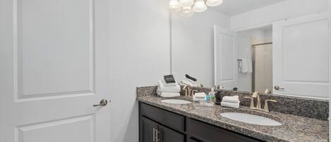 A bathroom with a double sink, dark cabinets, a large mirror, and a light fixture above the mirror.