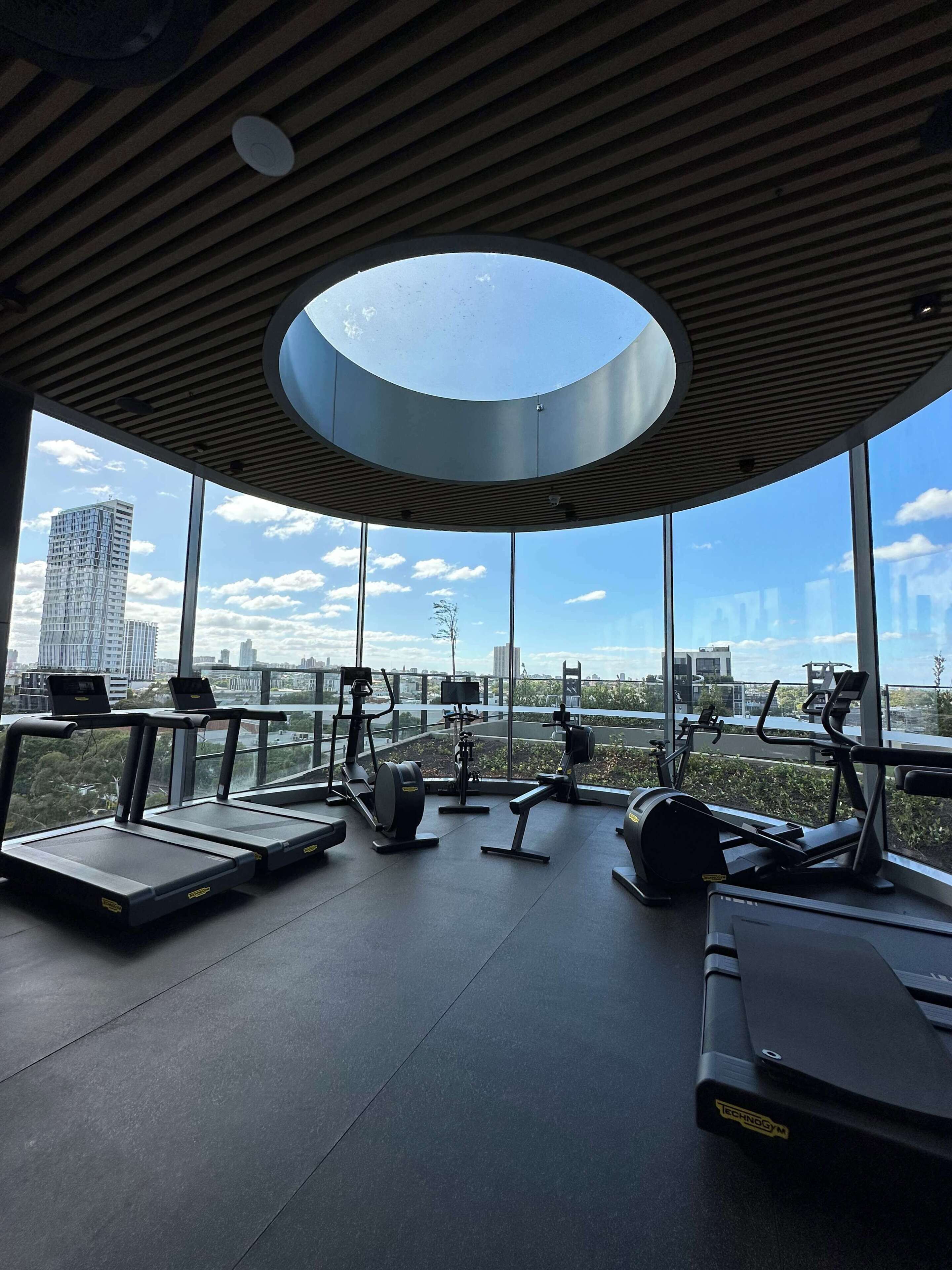 Ein Fitnessraum mit Trainingsgeräten und großen Fenstern mit Blick auf die Stadt.