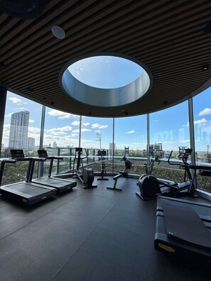 Ein Fitnessraum mit Trainingsgeräten und großen Fenstern mit Blick auf die Stadt.