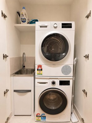 Ein kleiner Hauswirtschaftsraum mit einer gestapelten Waschmaschine und einem Trockner, einem Waschbecken und einem Regal mit Reinigungsmitteln.