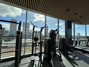 Ein Fitnessstudio mit Trainingsgeräten und großen Fenstern, die einen Blick auf die Stadt ermöglichen.
