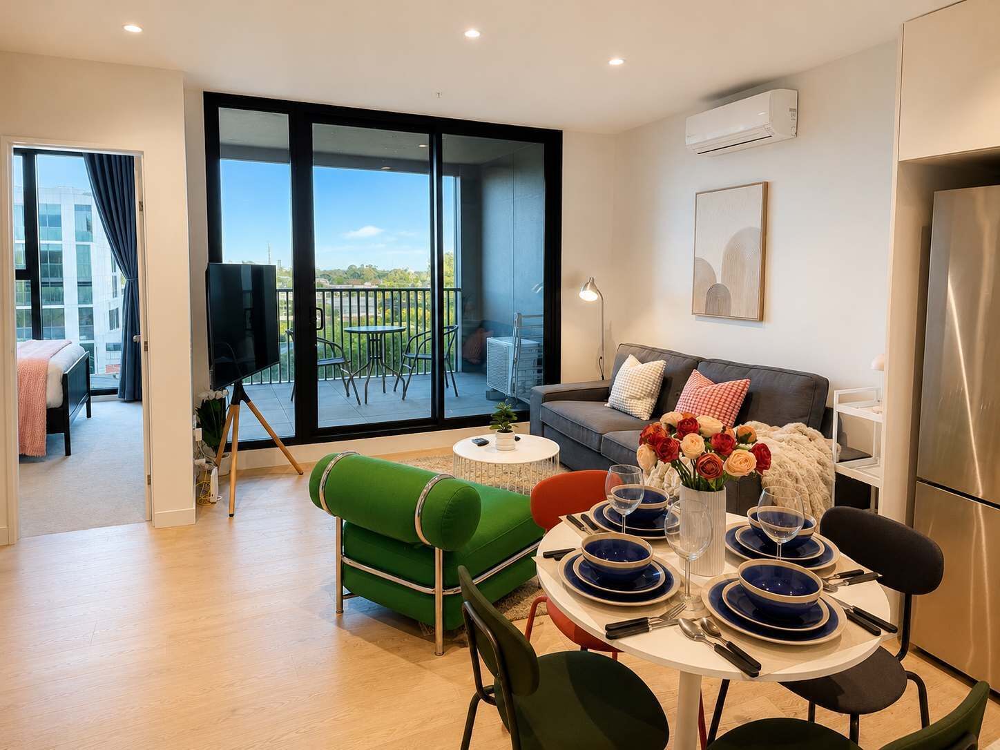 A modern living room with a balcony, a sofa, a dining table set, and a flat-screen TV.