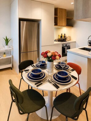 Eine moderne Küche mit einem Edelstahl-Kühlschrank, einem Esstisch gedeckt mit blauen Tellern und Weingläsern, und einer Vase mit roten und rosa Blumen.