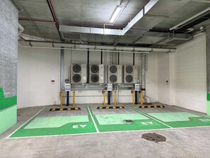 Ein überdachter Parkbereich mit Ladestationen für Elektrofahrzeuge, Klimaanlagen und einem Betonboden.
