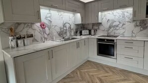 A modern kitchen with grey cabinets, a marble backsplash, and a herringbone wood floor. - Modern Top-Floor Flat — Crosby, Near Beach & Liverpool (Crosby)