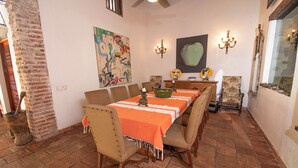 A dining area with a long table, multiple chairs, and a brick floor. - Casa Mejia (Cartagena de Indias)