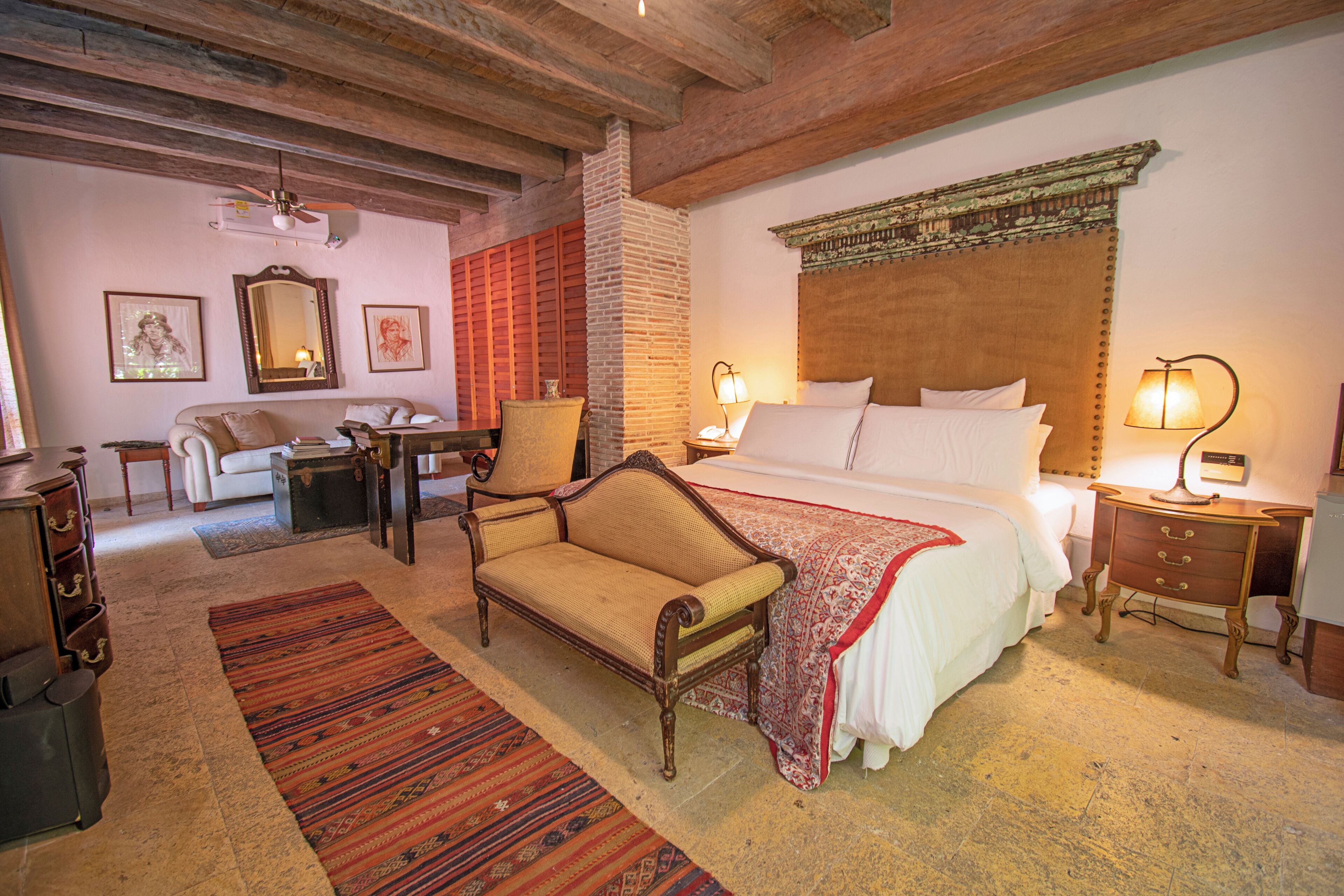 A traditional room with a bed, a sofa, a chair, a desk, and a lamp.