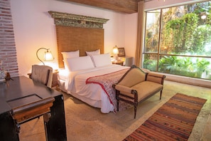 A bedroom with a bed, bedside tables, a chair, a window with a view of greenery, and a patterned rug. - Casa Mejia (Cartagena de Indias)