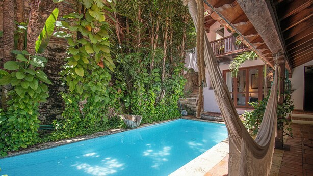 A swimming pool surrounded by lush greenery, a hammock, and a wooden deck. - Casa Mejia (Cartagena de Indias)