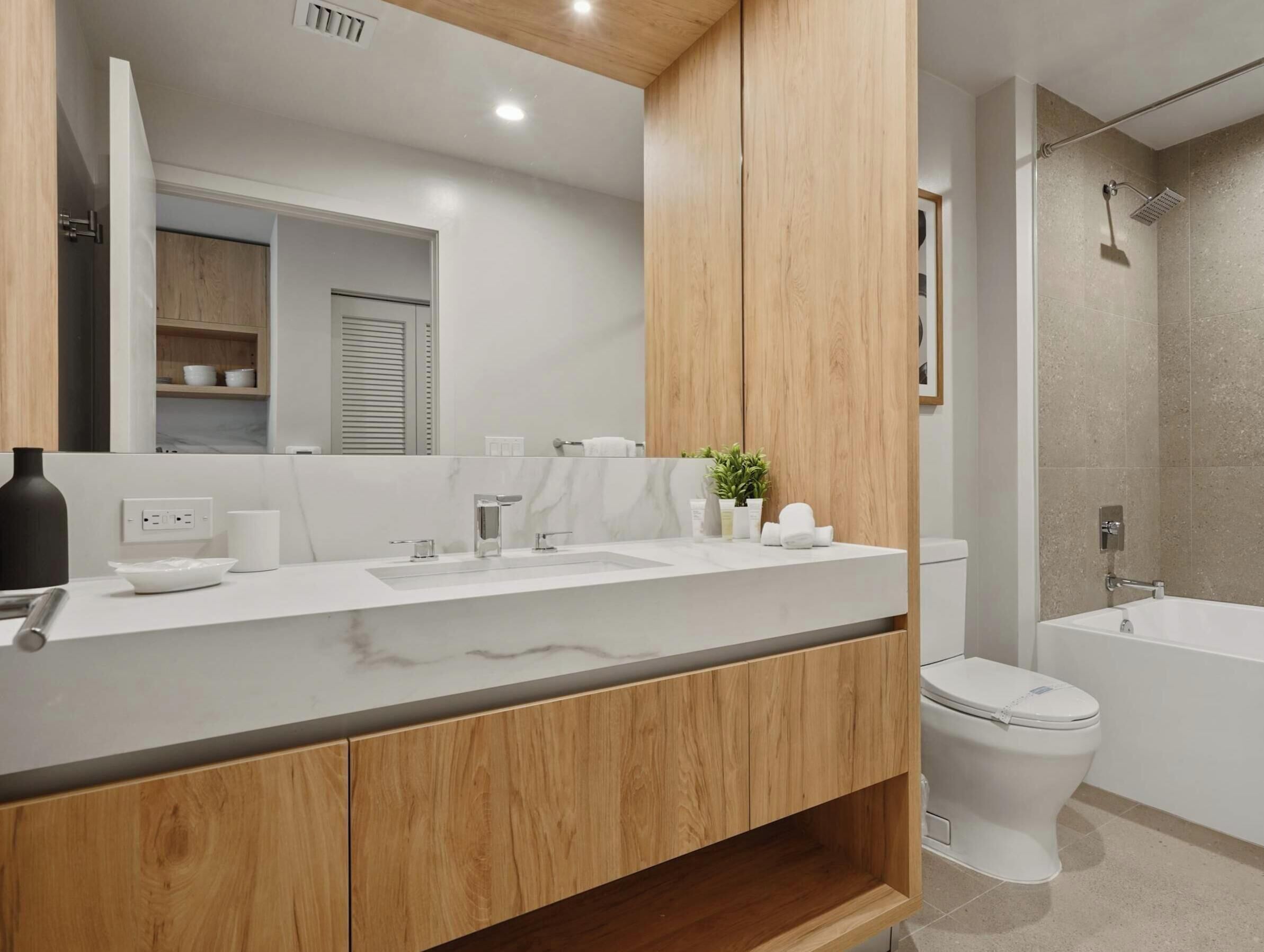 Un baño moderno con tocador de madera, un espejo grande, un lavabo blanco y una bañera.