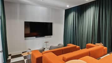 A modern living room with a flat-screen TV mounted on the wall, orange sofas, a small round table, and a checkered floor.