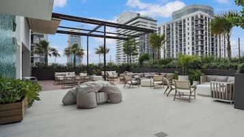 An outdoor seating area with multiple chairs and sofas, surrounded by greenery and under a pergola.