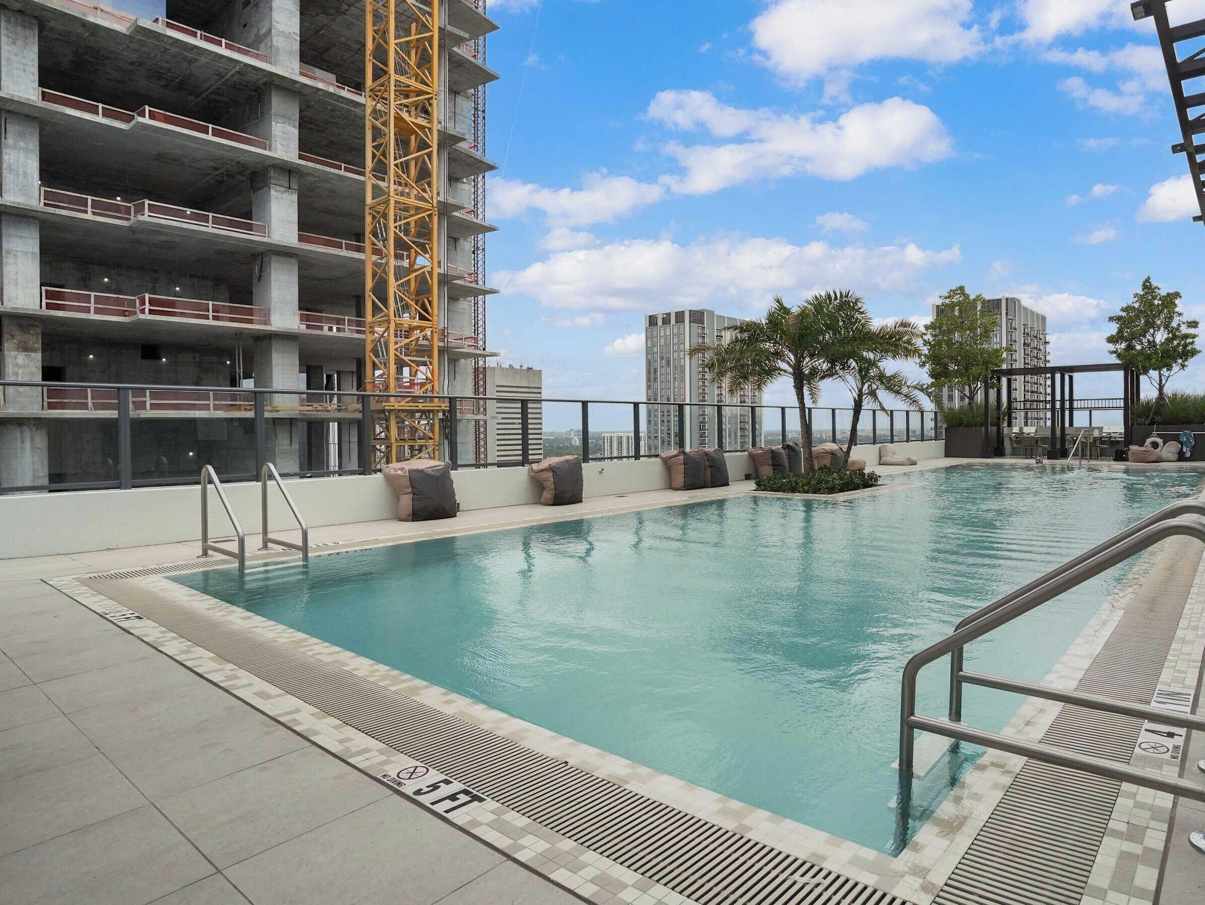 A swimming pool with a lifeguard stand, a poolside lounge area, and a view of a high-rise building under construction.