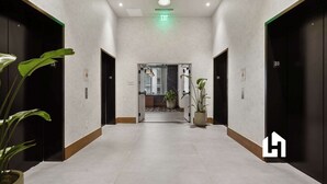 A hallway with two elevators, a green exit sign, and potted plants. - Downtown Studio with Pool, Gym & Movie Theater (Miami)