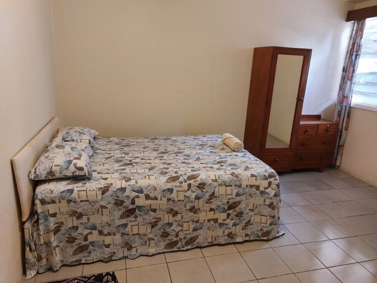 A small bedroom with a bed, a mirror, and a dresser.