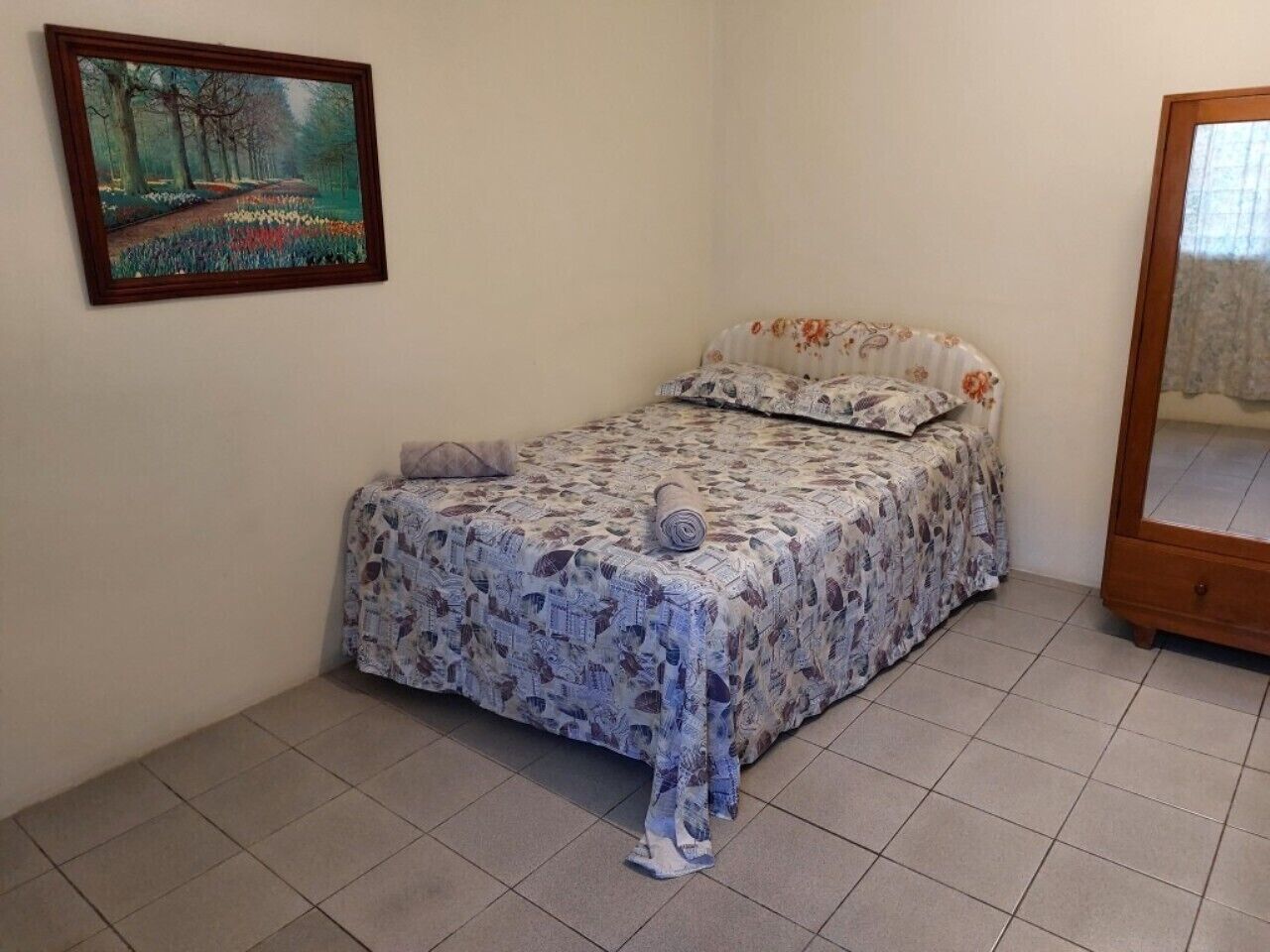 A small bedroom with a bed, a mirror, and a painting on the wall.