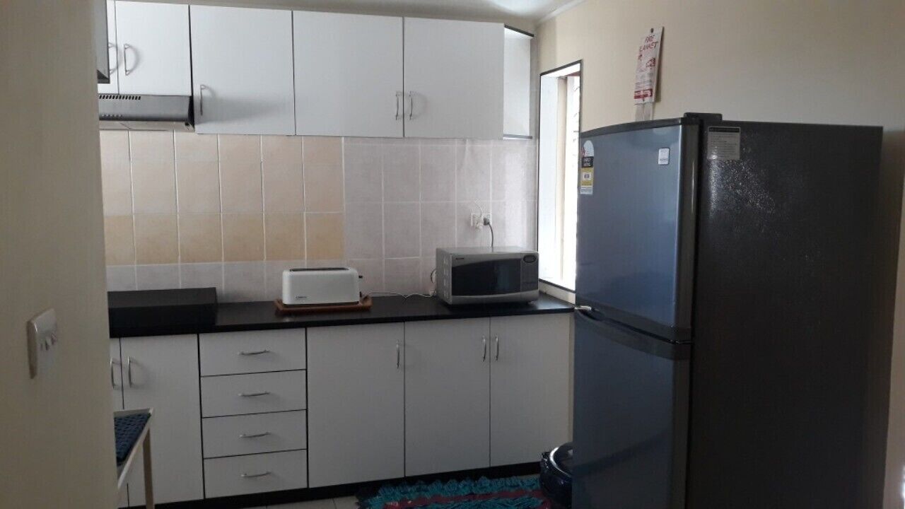 Una pequeña cocina con armarios blancos, un refrigerador negro, un microondas y un tostador.