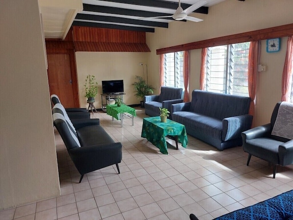 Uma sala de estar com sofá, cadeiras, televisão e ventoinha no teto.