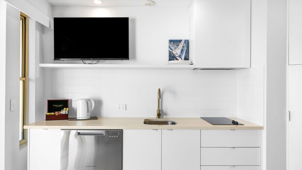 Una cucina moderna con lavastoviglie integrata, lavello in acciaio inossidabile e televisore a schermo piatto montato sopra il piano di lavoro.