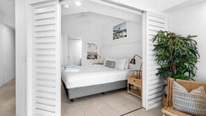 A bedroom with a bed, bedside table, lamp, and a large potted plant. - French Quarter 322 Beautiful One Bedroom Apartment (Noosa Heads)