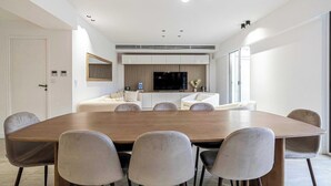 Una zona pranzo moderna con un grande tavolo in legno e sei sedie, una TV a incasso e un’area salotto con due divani.