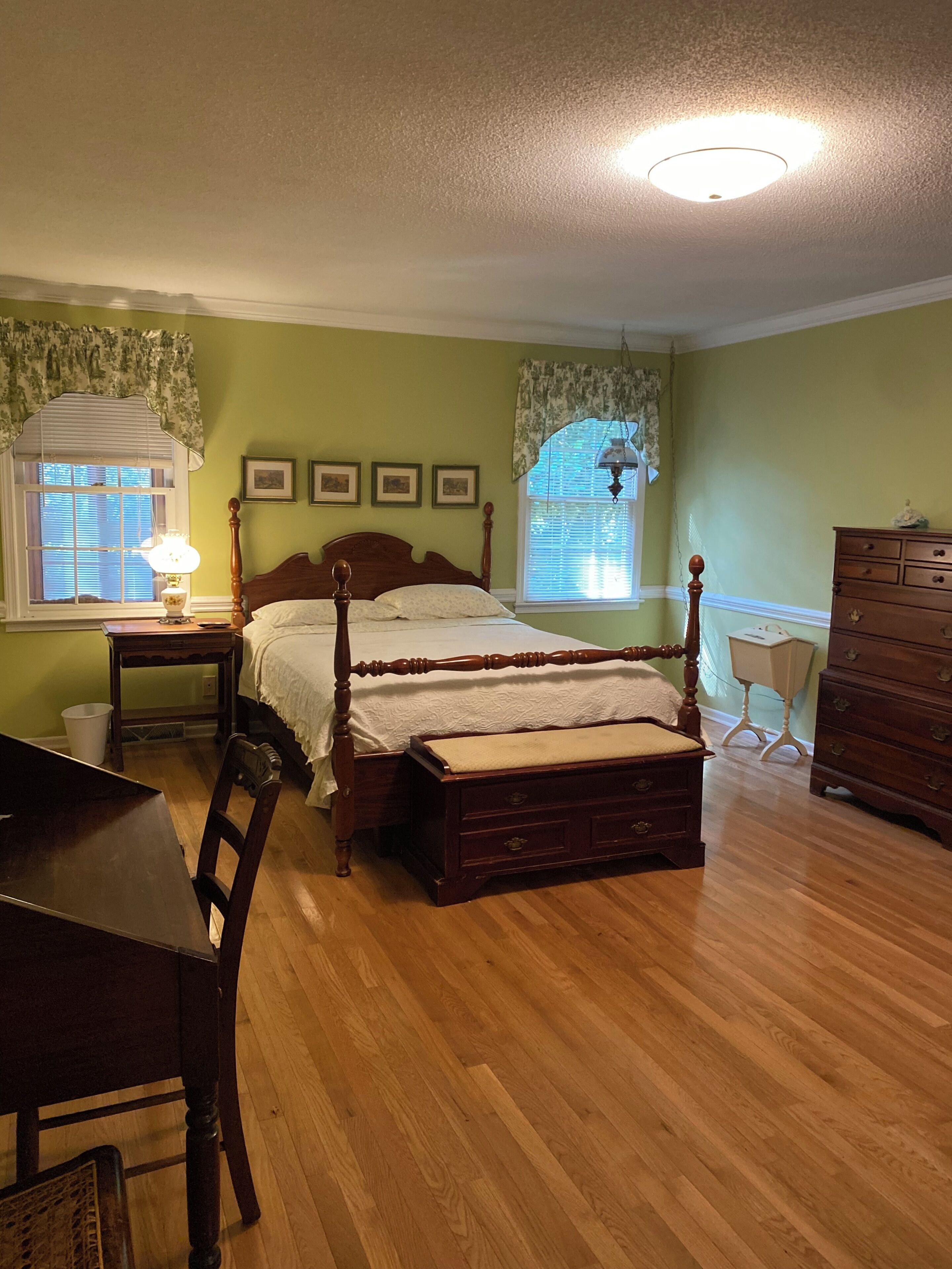 Een slaapkamer met een houten bed, een bureau, een stoel, een dressoir en een raam met gordijnen.