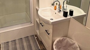 A modern bathroom with a glass shower enclosure, a white sink with two black cups, a mirror, and a trash bin. - The Banya Place - renovated cabin in Bright (Bright)