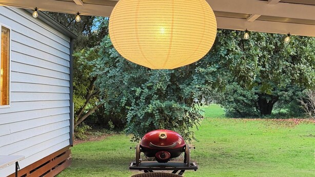 An outdoor patio with a wooden table, wicker chairs, and a hanging light fixture.