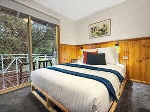 Un dormitorio con una cama grande, cabecera de madera, un cuadro en la pared y un balcón con vistas a árboles.
