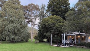 A house with a covered outdoor area, surrounded by trees and a well-maintained lawn. - The Banya Place - renovated cabin in Bright (Bright)